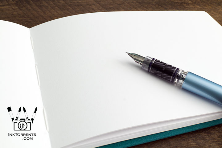 Fountain pen friendly notebook page with visible stitching and a blue fountain pen — InkTorrents Graphics